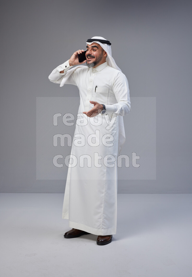 Saudi man Wearing Thob and white Shomag standing talking on phone on Gray background