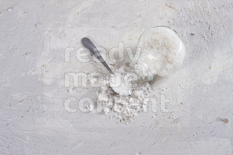 A glass jar full of coarse sea salt crystals on white background