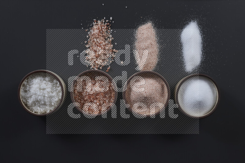 4 وعاء فخاري ممتلئين بملح الهيمالايا والملح الأبيض على خلفية سوداء