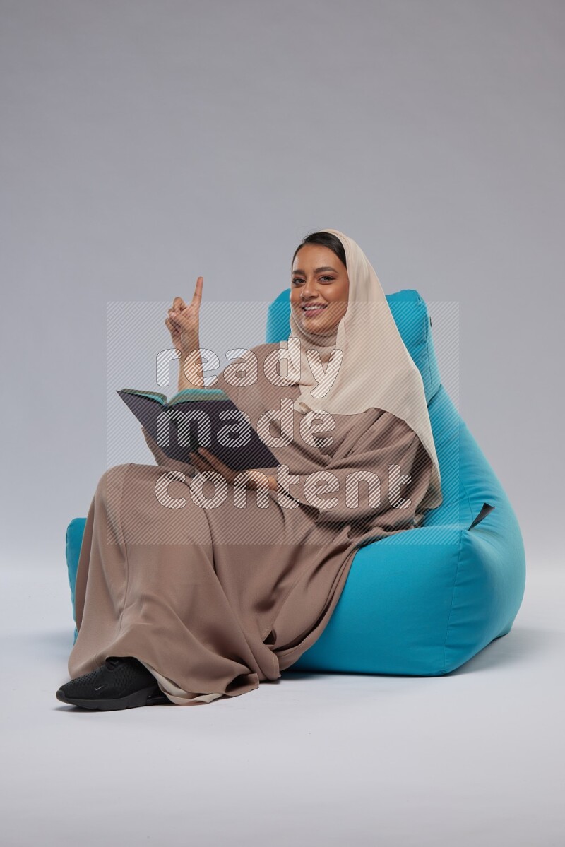 A woman sitting on a blue beanbag and reading a book