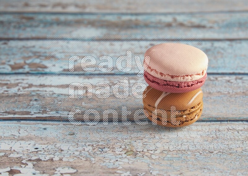 45º Shot of of two assorted Brown Irish Cream, and Pink Litchi Raspberry macarons on light blue background