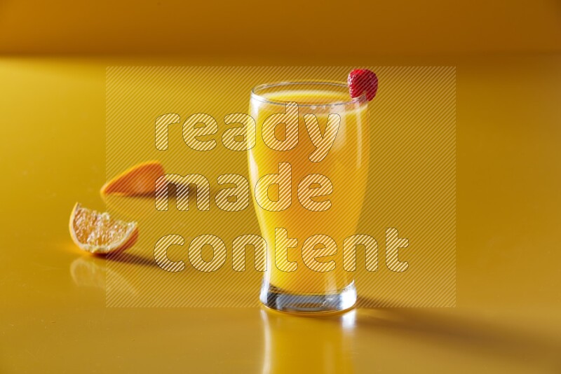 glass of orange juice with berry on yellow background