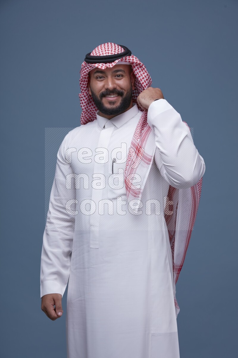 A Saudi man posing on blue background wearing Thob and Shomag