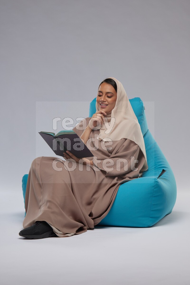 A woman sitting on a blue beanbag and reading a book
