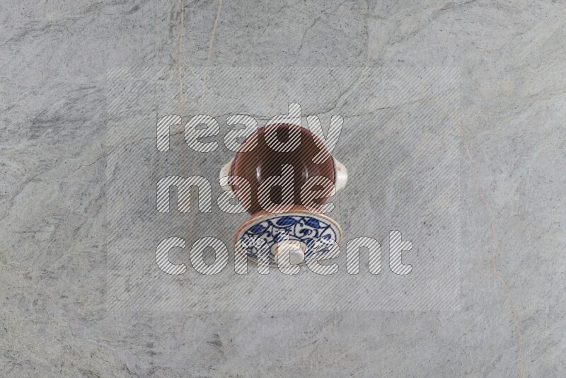 A multicolored pottery pot with its lid on grey marble background