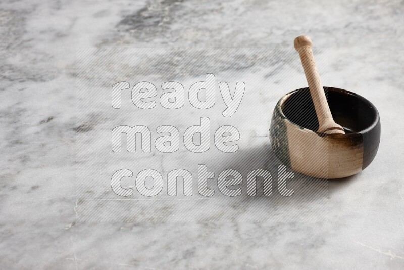 Multicolored pottery bowl with wooden honey dipper in it on grey marble background