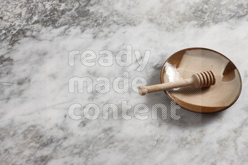 Multicolored pottery plate with wooden honey dipper in it on grey marble background