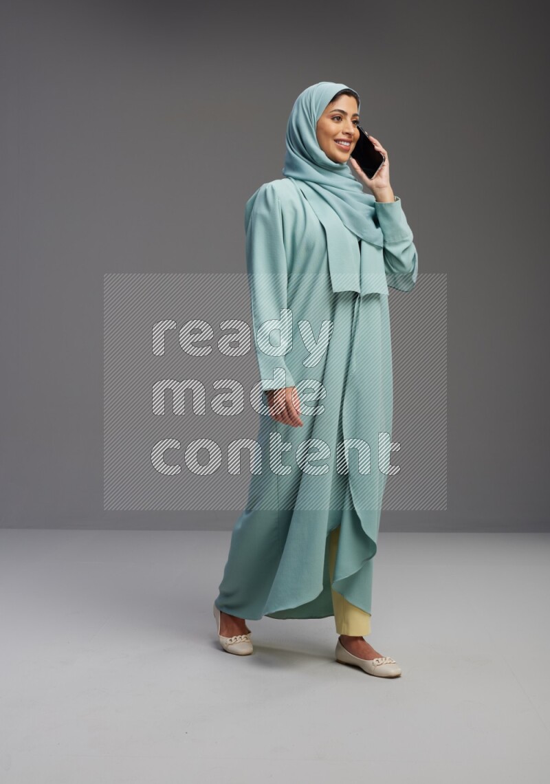 Saudi Woman wearing Abaya standing talking on phone on Gray background