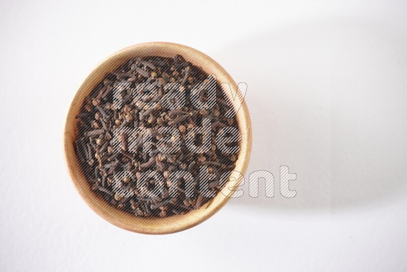 A wooden bowl full of cloves on a white flooring