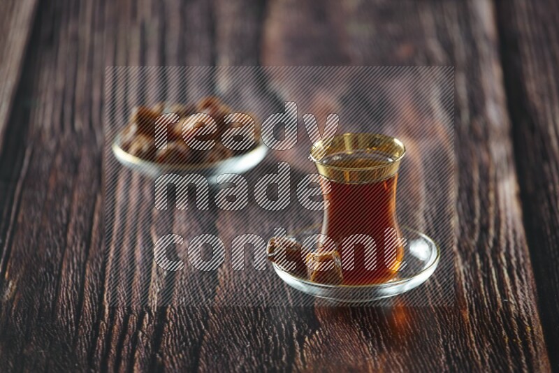 A tea glass cup with dates and coffee on wooden background