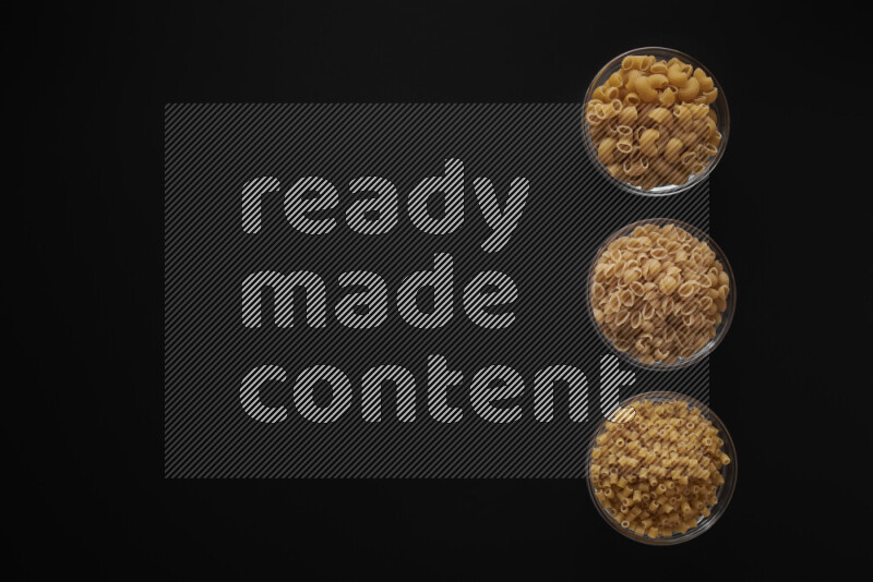 Different pasta types in 3 glass bowls on black background