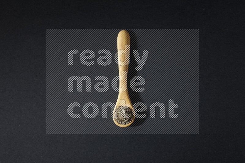 ملعقة خشبية ممتلئة بحبوب الكمون على خلفية سوداء