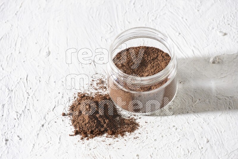 A glass jar full of cloves powder on a textured white flooring