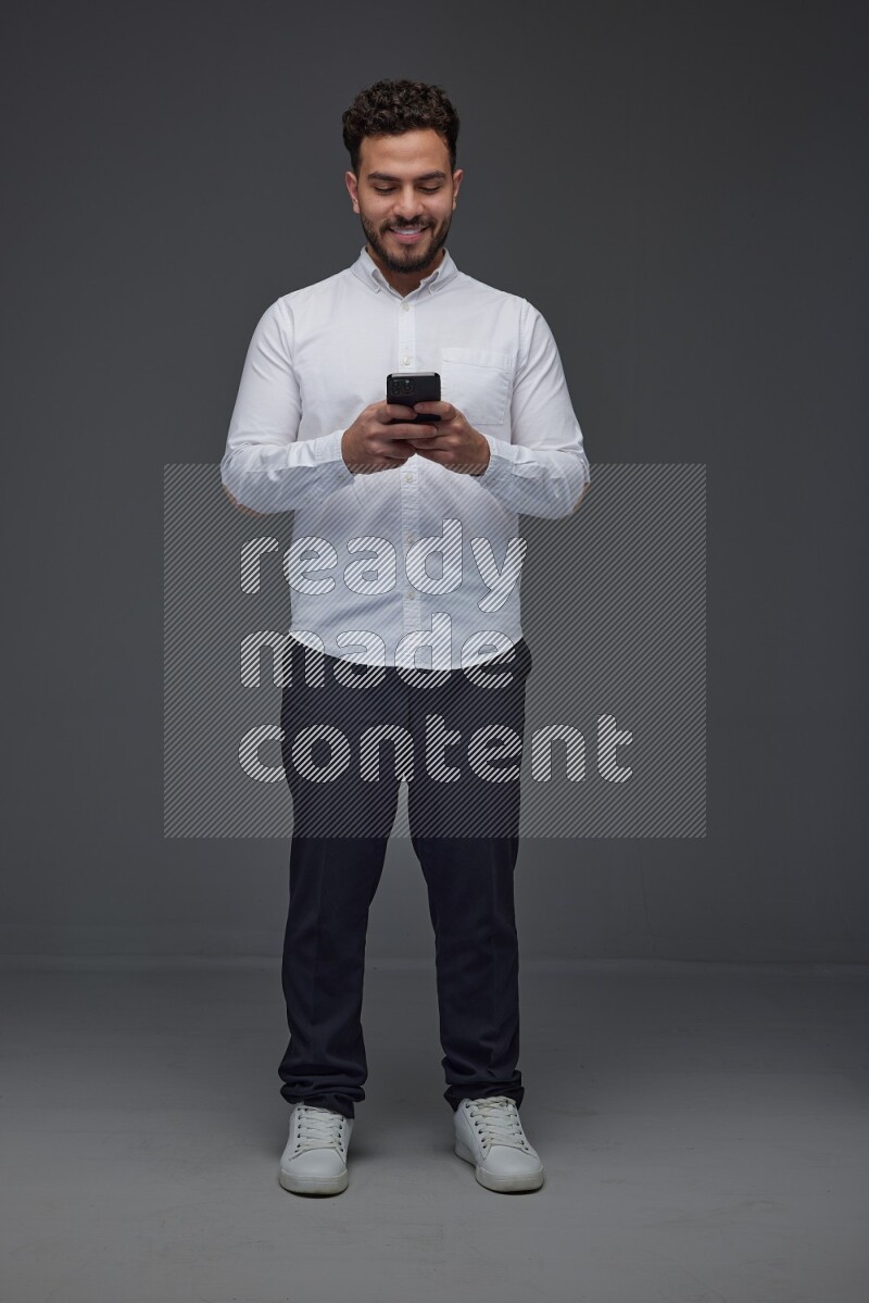 A man wearing smart casual standing and using his phone eye level on a gray background