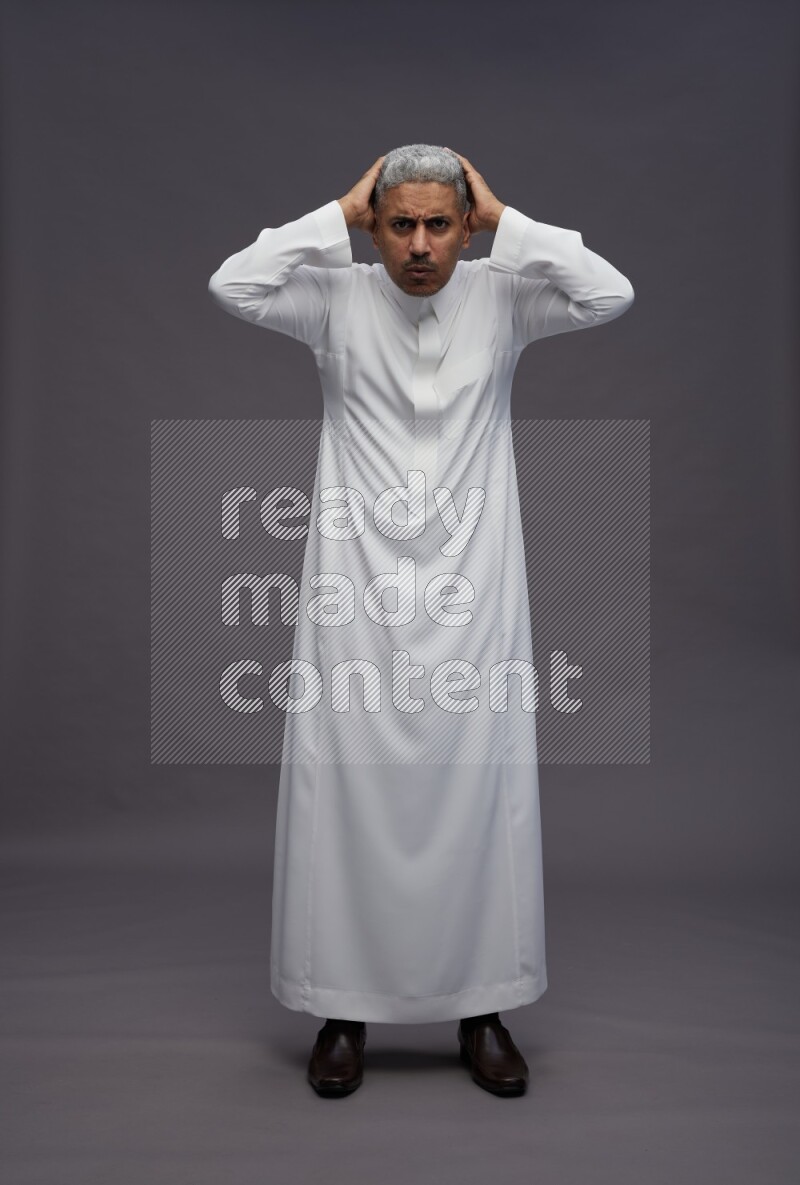 Saudi man wearing thob standing hands behind head on gray background