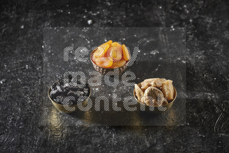 فواكه مجففة في أطباق معدنية علي خلفية سوداء خشبية