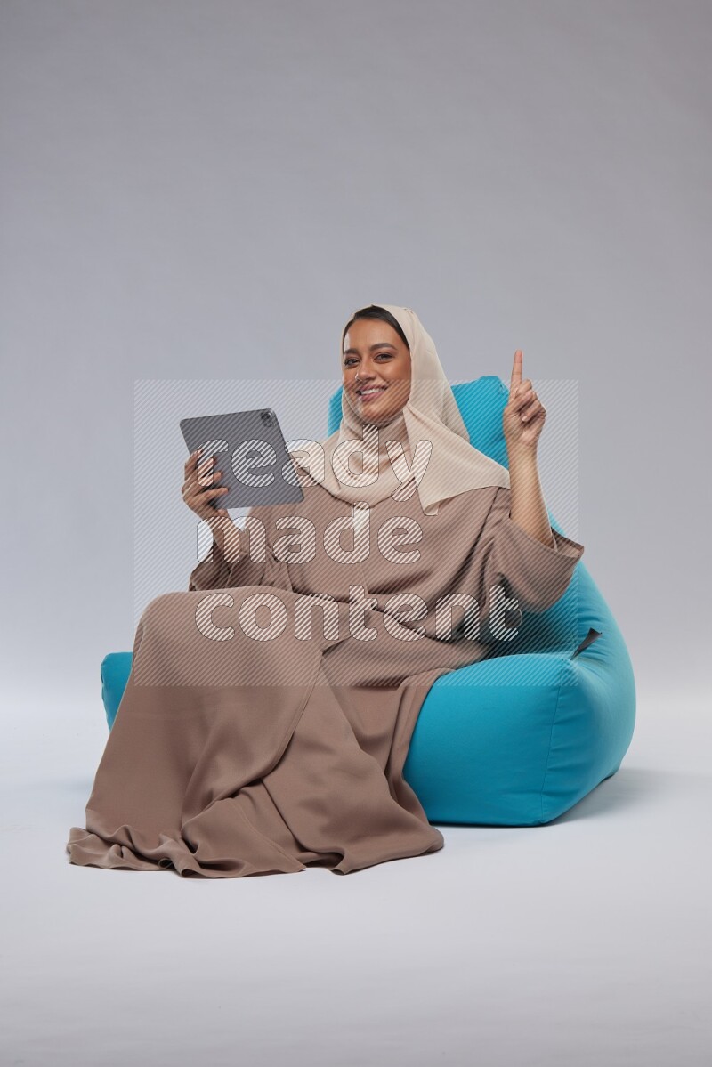 A Saudi woman sitting on a blue beanbag and working on tablet