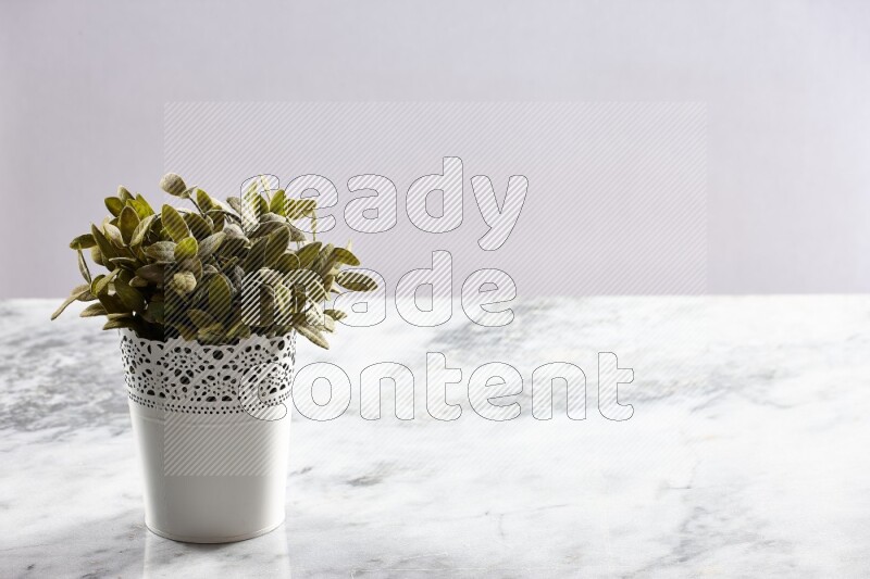 Green artificial plant in white decorative pot on grey marble background