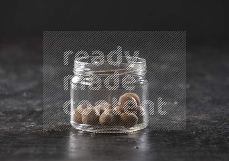 A glass jar full of whole nutmeg seeds on a black flooring