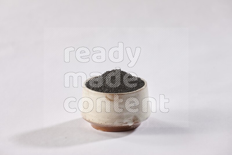 A beige pottery bowl full of black seeds on white flooring