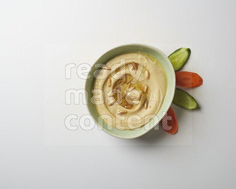 Hummus in a green plate garnished with pine nuts on a white background