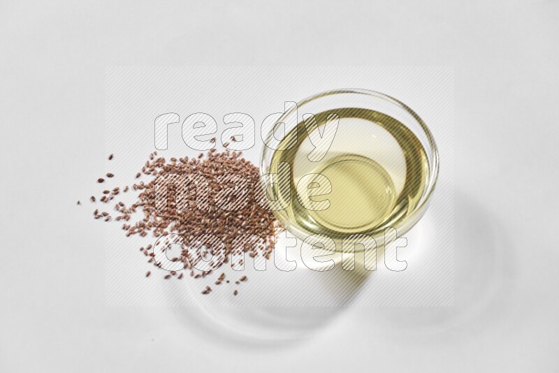A glass bowl full of flaxseeds oil and flaxseeds beside it on a white flooring