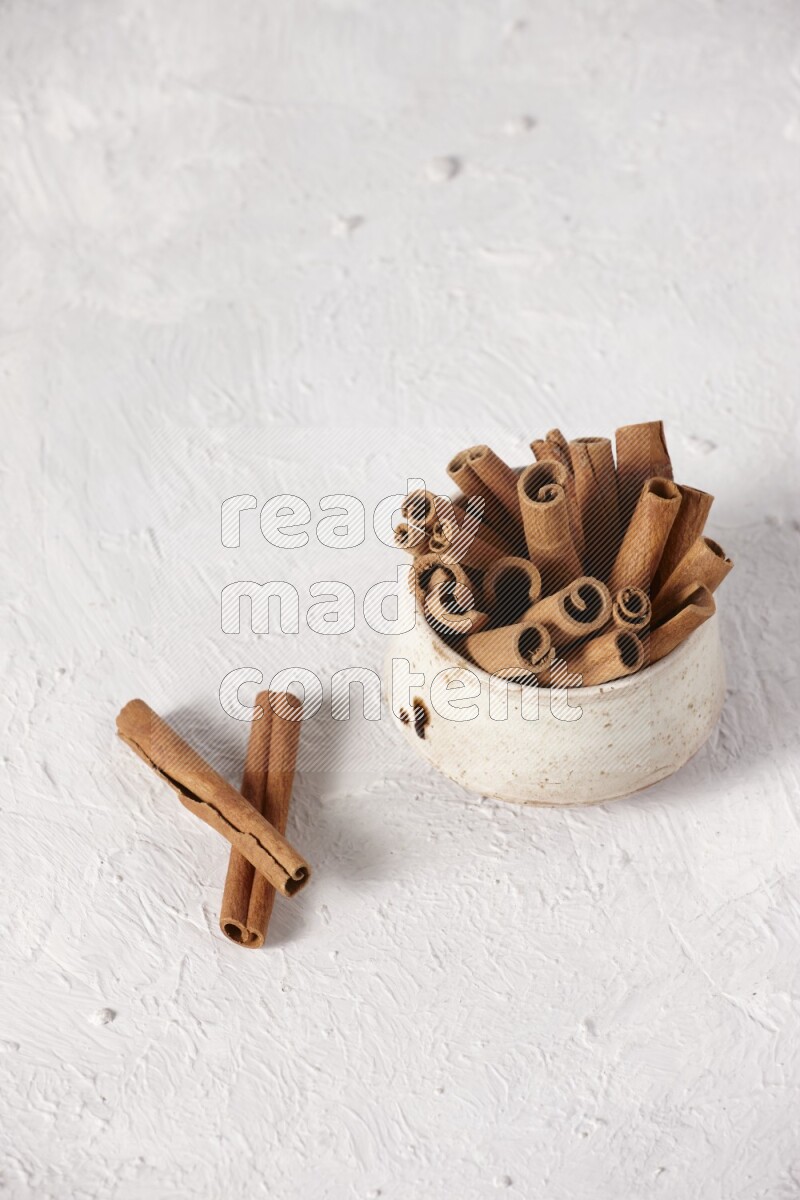Cinnamon sticks in a beige bowl on a white background