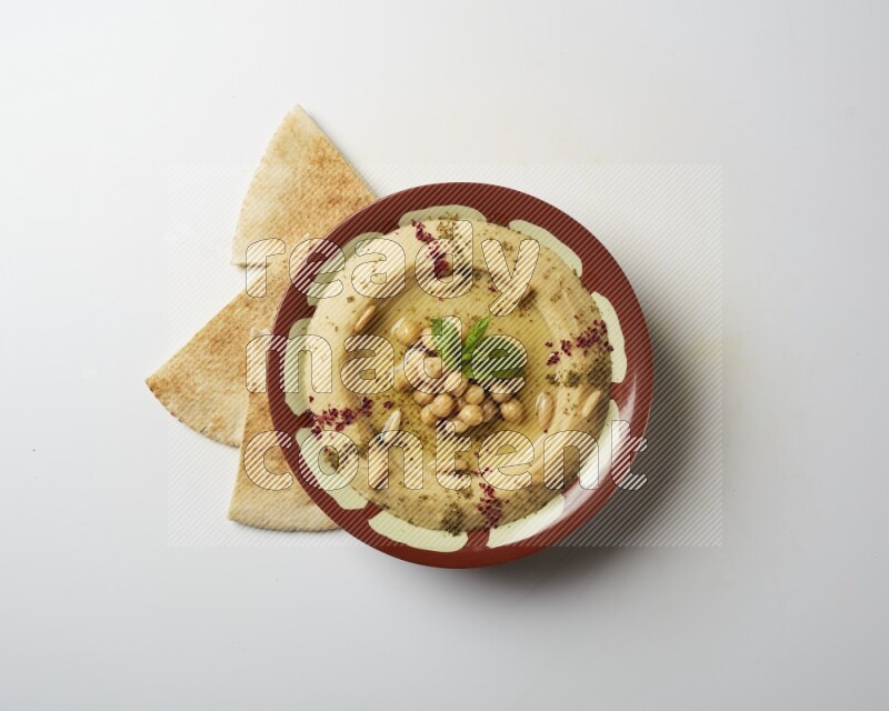 Hummus in a traditional plate garnished with zaatar & sumak on a white background