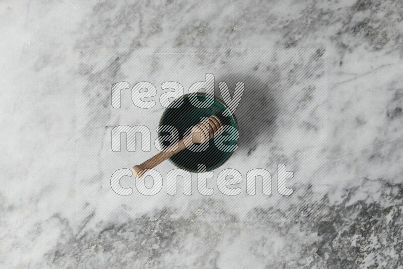Dark green pottery bowl with wooden honey dipper in it on grey marble background