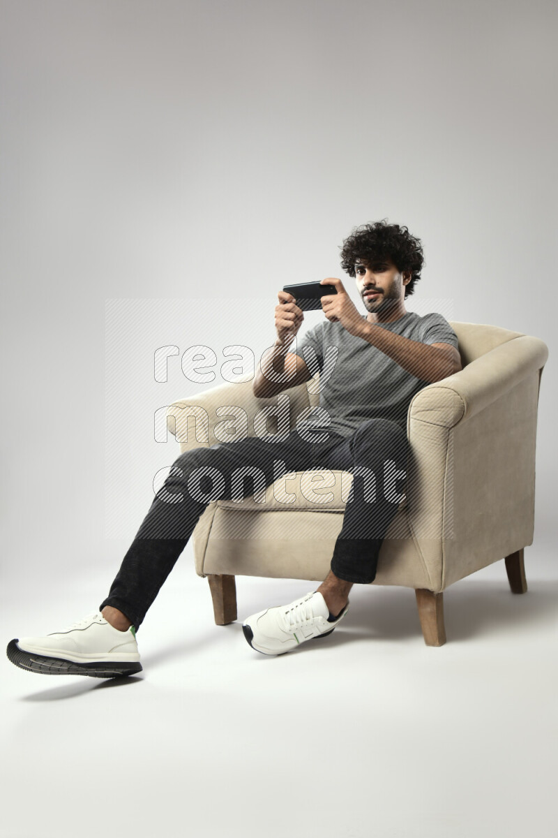 A man wearing casual sitting on a chair gaming on the phone on white background