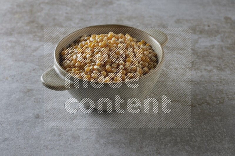 corn kernel in a off-white handheld ceramic bowl on a grey textured countertop