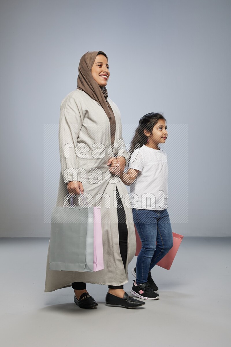 Mom and daughter holding shopping bags on gray background