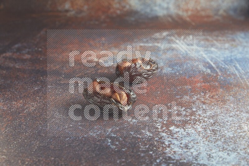 two hazelnut stuffed madjoul dates on a rustic reddish background