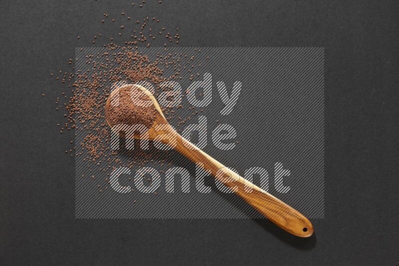 A wooden ladle full of garden cress seeds and seeds spread beside it on a black flooring