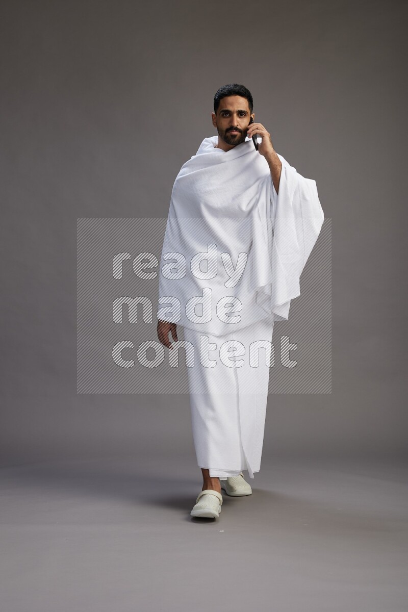 A man wearing Ehram Standing talking on phone on gray background