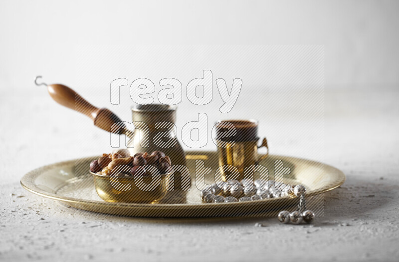 Nuts in a metal bowl with coffee and prayer beads on a tray in a light setup