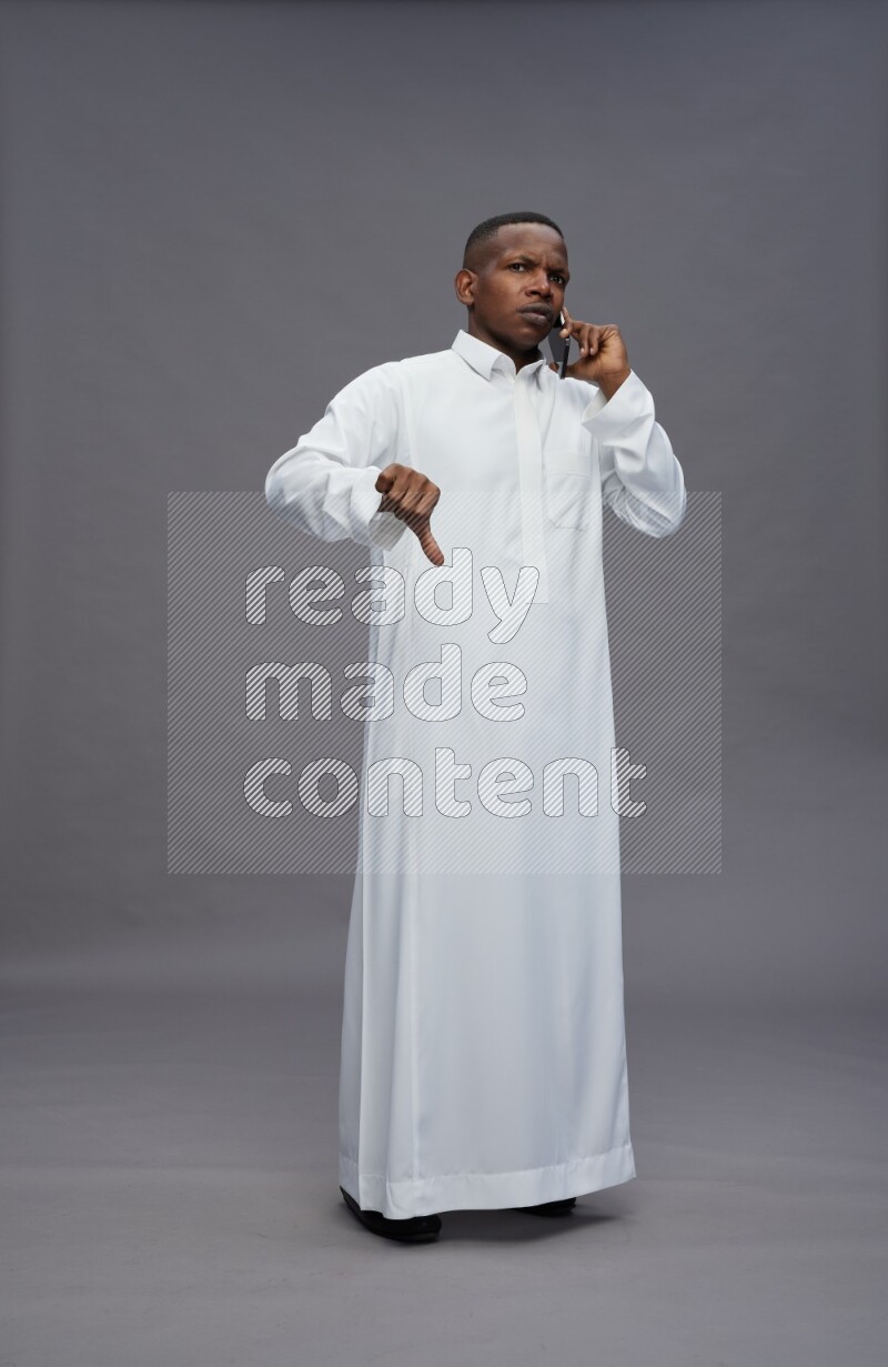 Saudi man wearing thob standing talking on phone on gray background
