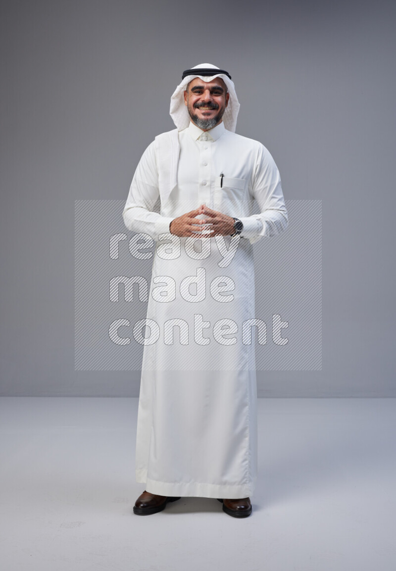Saudi man Wearing Thob and white Shomag standing interacting with the camera on Gray background
