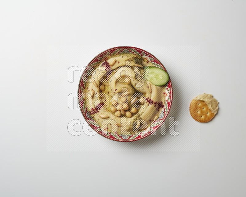 Hummus in a red plate with patterns garnished with zaatar & sumak on a white background