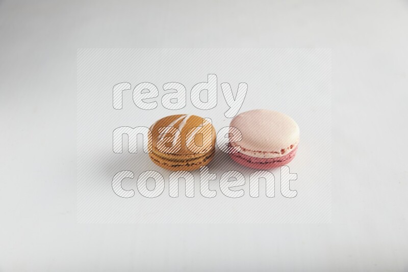 45º Shot of of two assorted Brown Irish Cream, and Pink Litchi Raspberry macarons on white background