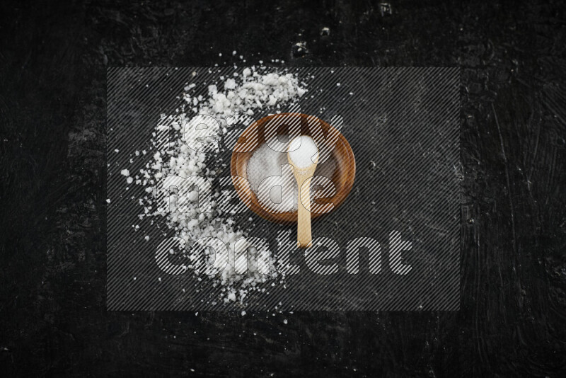 A pottery plate full of fine salt with bunch of coarse salt beside it on black background