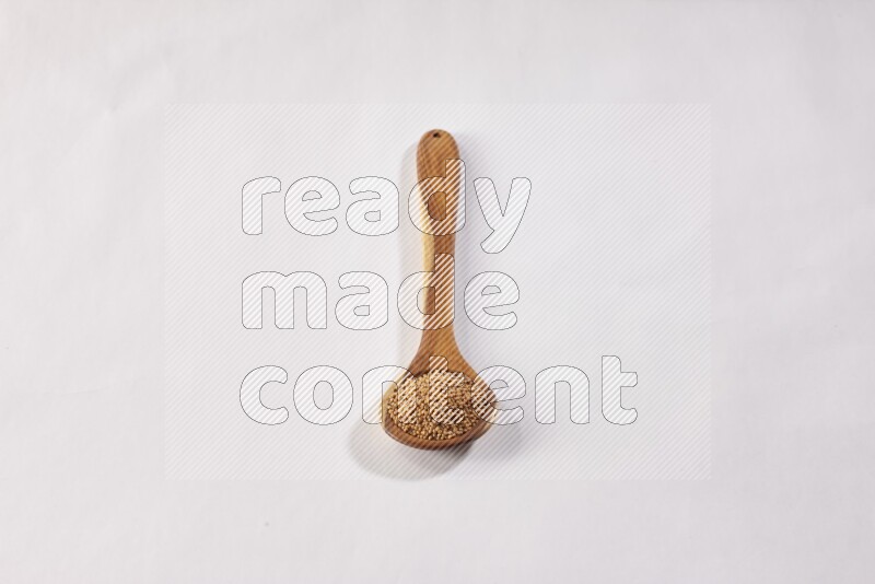 A wooden ladle full of mustard seeds on a white flooring