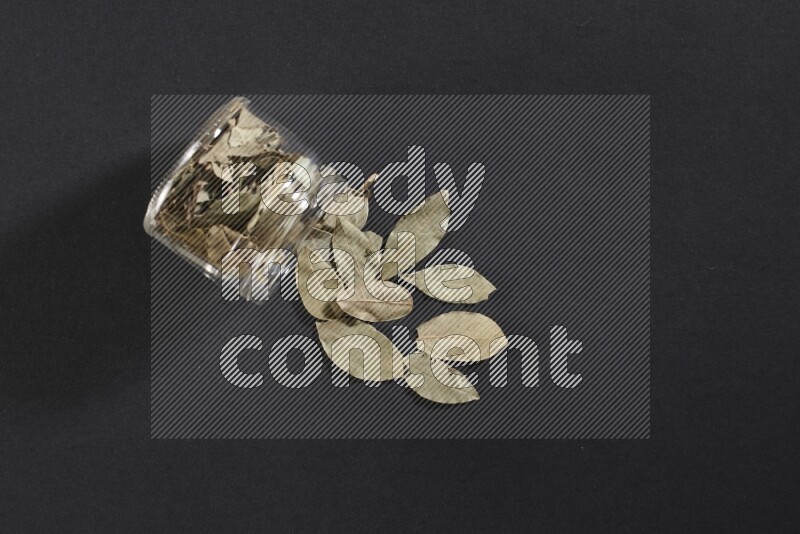 وعاء زجاجي ممتلئ بأوراق الغار والوعاء مقلوب وبعض الأوراق متناثرة خارجه علي خلفية سوداء