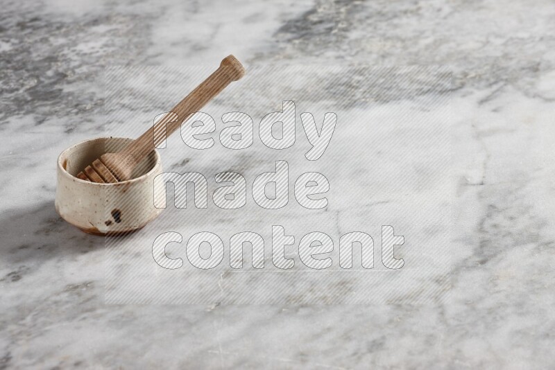 Beige pottery bowl with wooden honey dipper in it on grey marble background