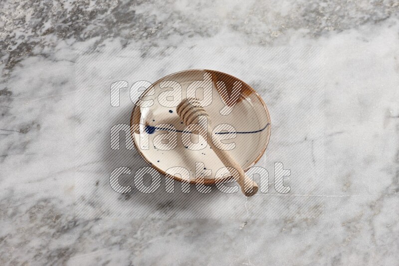 Multicolored pottery plate with wooden honey dipper in it on grey marble background