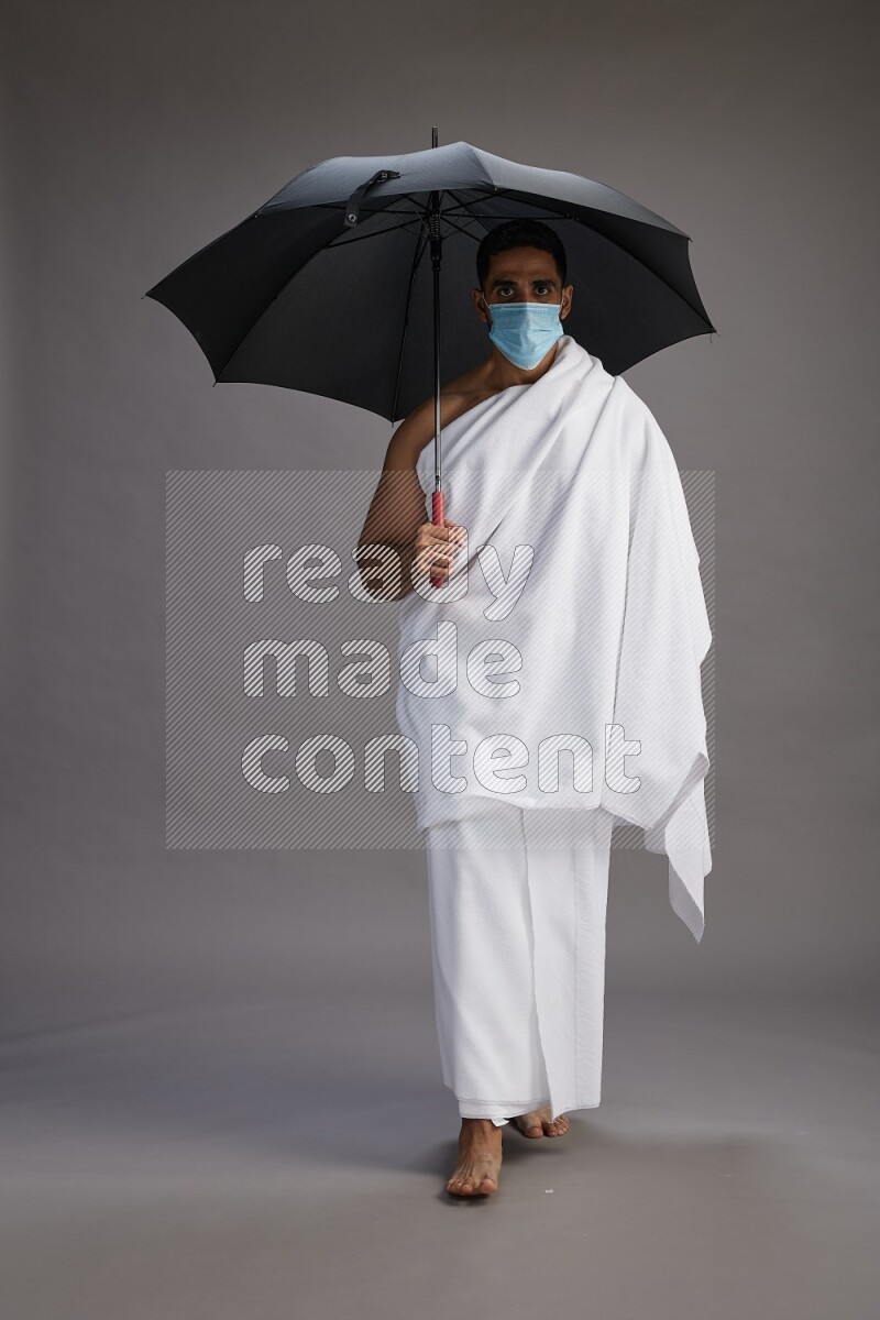 A man wearing Ehram and mask Standing holding umbrella on gray background on gray background