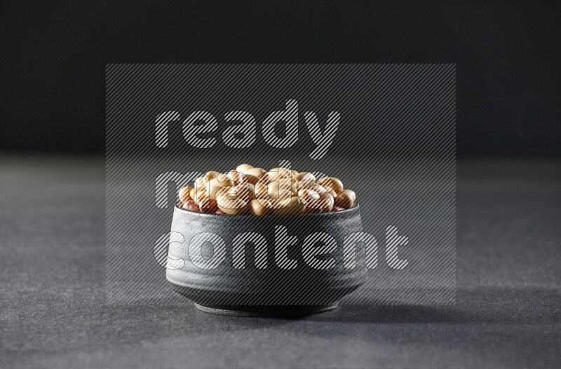A black pottery bowl full of peeled peanuts on a black background in different angles