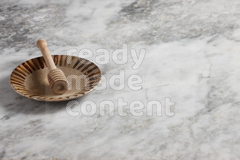 Multicolored pottery plate with wooden honey dipper in it on grey marble background