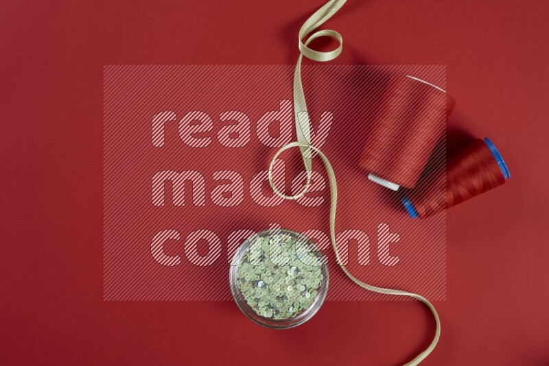 A green and red collection of sewing and tailoring tools arranged on a red background