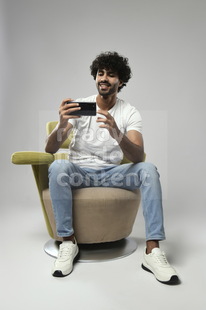 A man wearing casual sitting on a chair shooting with his phone on white background
